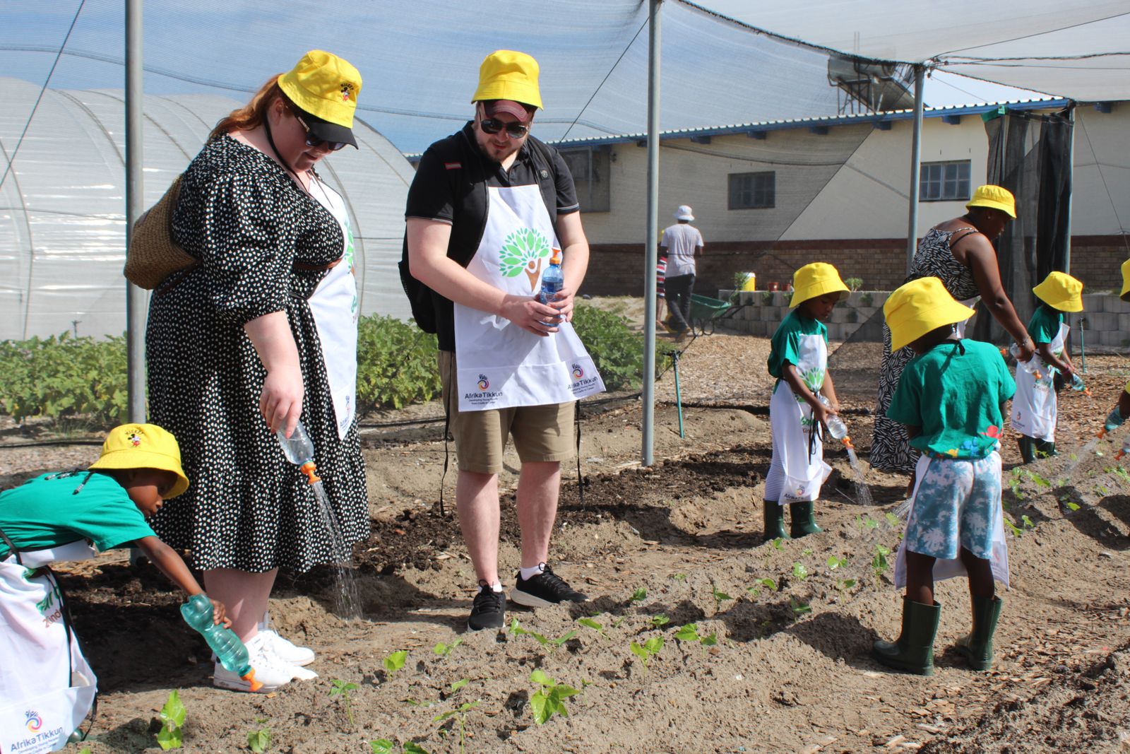 Children in yellow hats gardening with adult volunteers